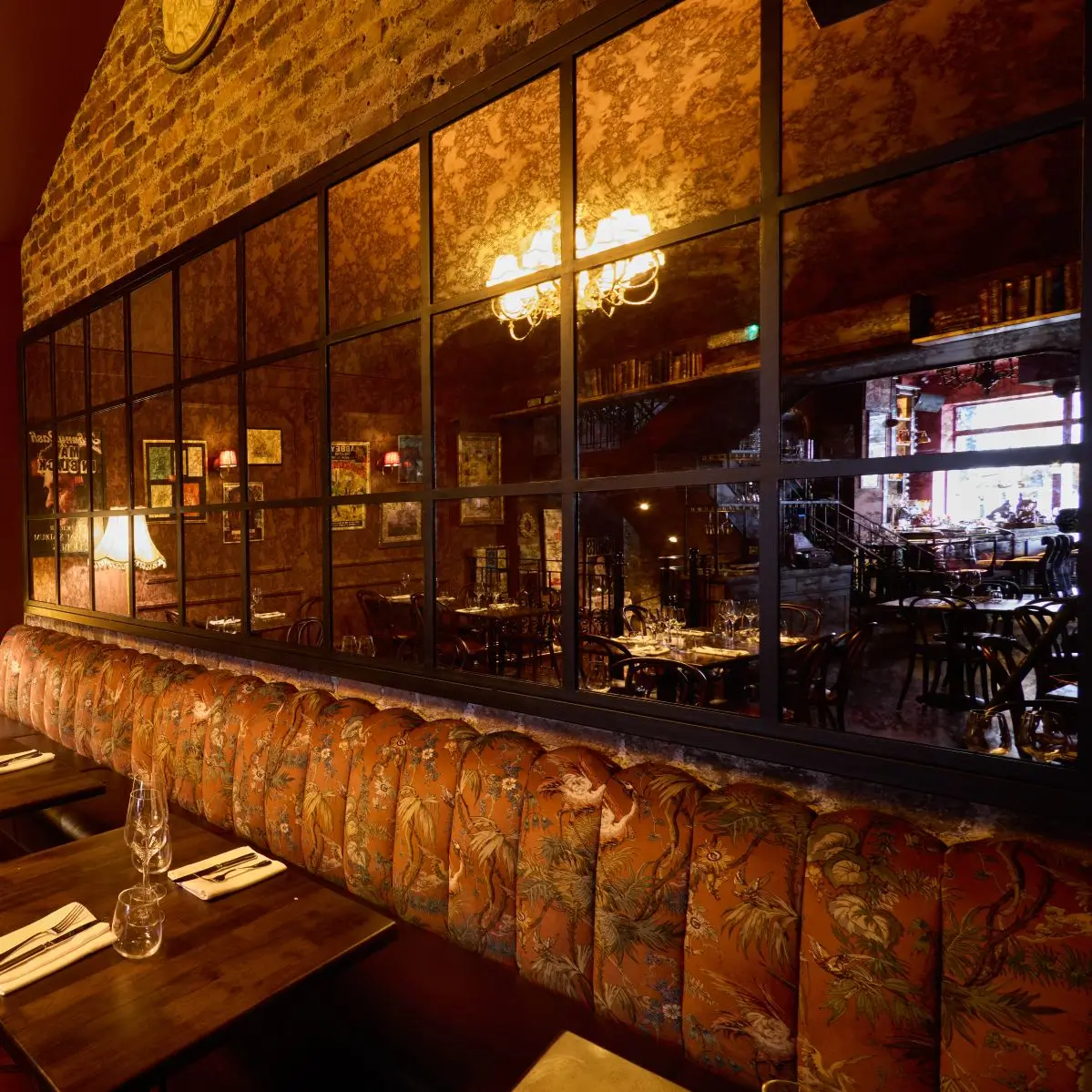 Home 4 The warm interior of Fitzers Bistro, showing a plush, patterned banquette seat against an exposed brick wall and a large feature mirror reflecting the cozy dining room.