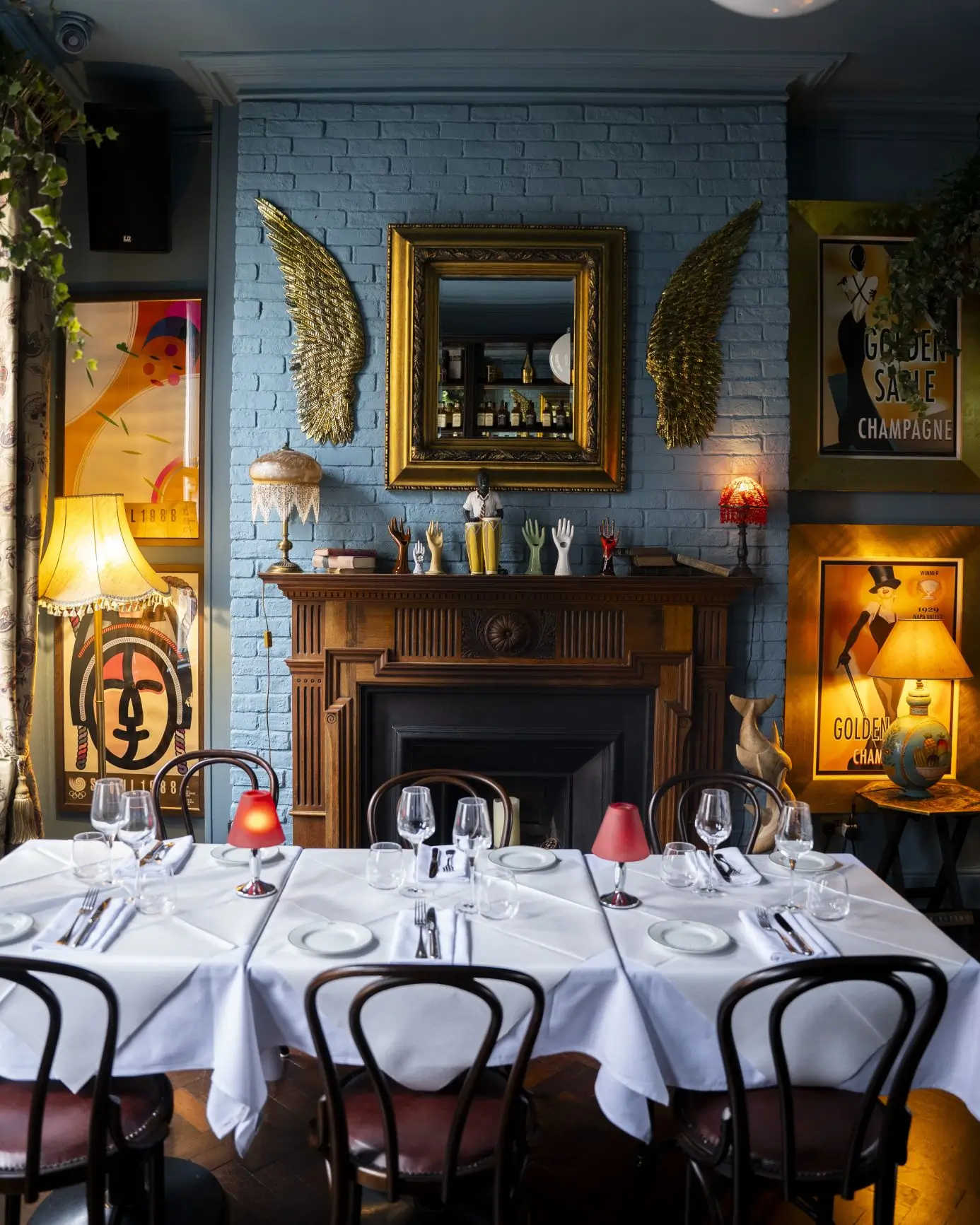 A close-up of the feature fireplace in the Blue Room at Fitzers Bistro, decorated with golden wings, a large mirror, and eclectic art.